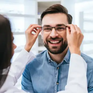 Man smiling while adjusting glasses in a professional setting