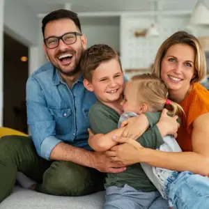 A family of four sitting together on a couch, smiling and hugging each other.