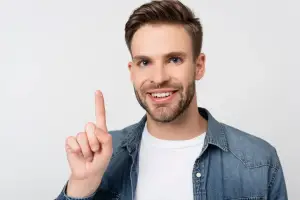 A smiling man with a beard pointing at a white background with his index finger