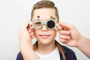 A young boy wearing glasses with a cross symbol on the side, being examined by a person.