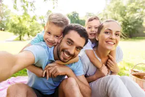 A family of four, two kids and two adults, sitting on a grassy field with a picnic basket and smiling for a photo