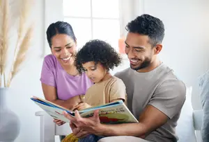 A family with a young boy and his parents are sitting on a couch and reading a book