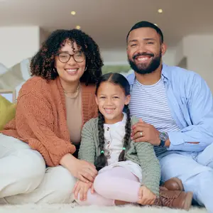 A family sitting on the floor with a girl smiling in between a man and a woman