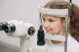 A young girl is looking through an eye examination machine