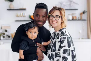 A man holding a baby smiles with a woman wearing glasses