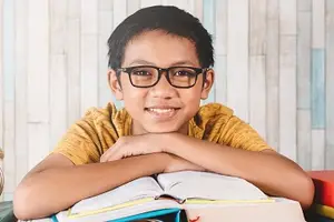 A boy with glasses sitting at a desk with books in front of him