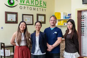 Four individuals stand in front of a sign reading Warden Optometry, smiling for a photo.