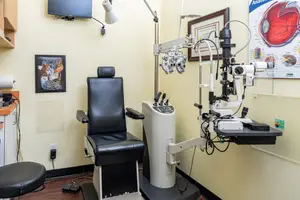 An optometrist's room with a chair, medical equipment, and a mounted television.