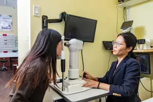 An optometrist is examining a patient's eyes using a slit lamp in a well-lit clinic.