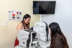 Two women are examining an eye imaging machine in an optometrist's office.