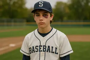 A baseball player with a bruise under his eye stands on a baseball field wearing a baseball uniform and a hat.