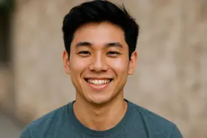 A smiling man with short black hair wearing a blue shirt is looking forward in a photo with a blurred background.
