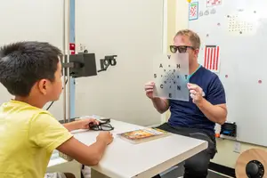 A man is conducting an eye exam on a young boy in a clinical setting.