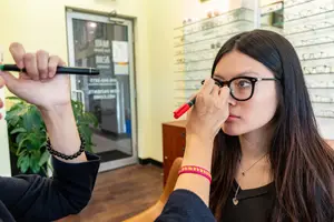An optometrist is adjusting a young woman's glasses with a marker and a pencil.