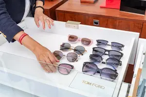 A person is browsing through a display case of Tom Ford sunglasses, which includes various shades such as pink, black, and gray, with the brand name clearly visible.