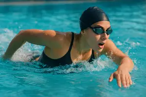 A woman wearing a black swimsuit and goggles is swimming in a pool.