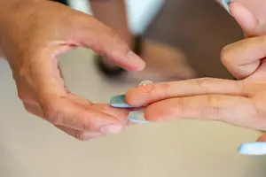 Two hands with one holding a contact lens between their fingers