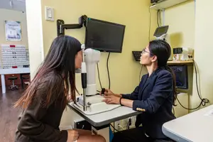 A woman uses an eye exam machine in an optometrist's office.
