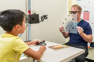 An optometrist is examining the vision of a young boy wearing glasses in an examination room