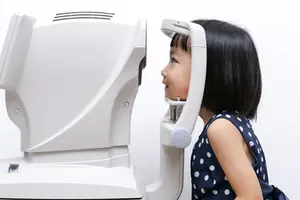 A young girl is sitting on a chair and using an eye test machine in a white room