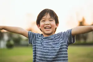 Close-up of a happy young boy with arms outstretched standing in a grassy field.