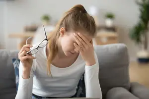 woman with headache holding glasses in living room