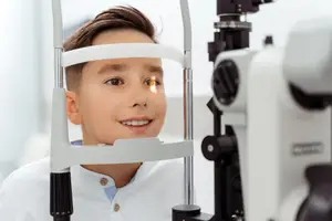 A young boy is smiling while looking through an eye exam machine.