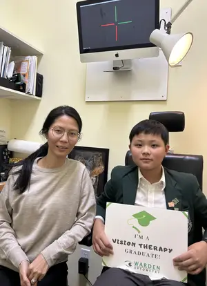 Woman and boy pose with sign for Vision Therapy Graduate in front of computer