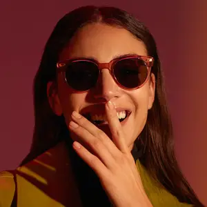 Woman wearing sunglasses and a green jacket smiles and poses for a photo