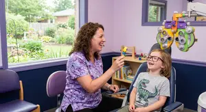 A woman and a child in a dental clinic with a purple wall and window with a view of the garden outside