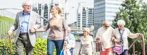 A group of older people are holding hands and walking on the street in front of a building.