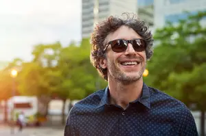 Man smiling in sunglasses and a blue shirt on a city street