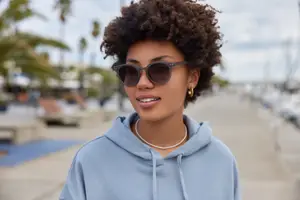 A smiling woman wearing sunglasses and a blue hoodie on a pathway