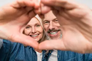 A man and woman are smiling and posing for a photo with their hands in a heart shape