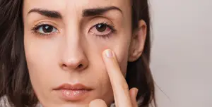 A woman with brown eyes and eyebrows is touching her eye with her finger while looking at something
