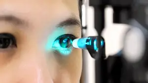 A close-up view of a woman's eye with a blue light shining on it, likely during an eye examination.