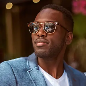 A man wearing a denim blazer and sunglasses is standing outside and looking to the left.