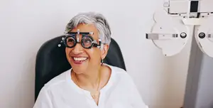 A smiling woman wearing glasses and sitting in front of an eye examination machine
