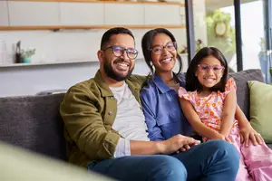 A man, a woman, and a young girl are sitting on a couch together, smiling and posing for a picture.
