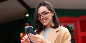 A woman with glasses holding a cell phone in front of a red door