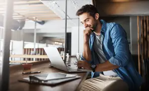 A smiling man working on a laptop in a room with wooden walls