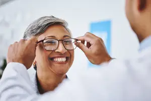 An older woman with gray hair smiling while holding a pair of glasses in her hands