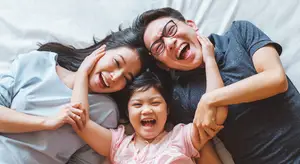 Three people lying on a bed with a child in the middle laughing
