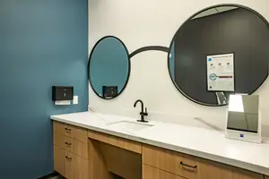 An interior shot of a bathroom with two round mirrors, a sink, and a tissue dispenser.