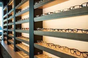 A collection of glasses displayed on shelves in a store, with a few on the floor as well, arranged in rows and columns, showcasing various frames and lenses.