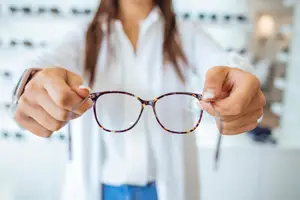 A woman in a white shirt holds a pair of eyeglasses in her hands, possibly in a shop.