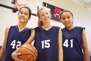 Three girls wearing blue jerseys with numbers 42, 15, and 41 are smiling and posing for a photo in a basketball court.