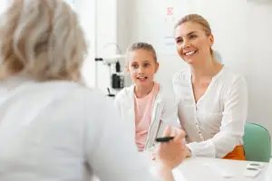 A woman and a young girl sitting in front of a table, probably in a clinic, and the woman is looking at the girl while smiling