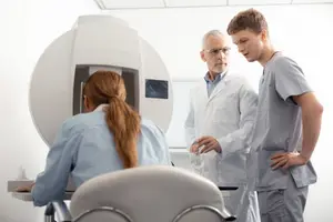 An older man and two younger individuals are standing around a medical device in a clinic.