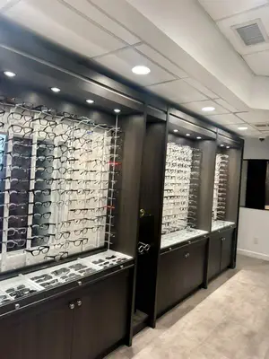 An indoor display of eyeglasses with a wooden cabinet and white walls, illuminated by ceiling lights.